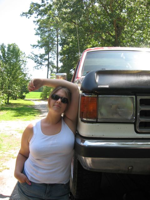 1987 Ford Bronco - A woman leans against the front corner of a white and red truck with a black hood scoop.