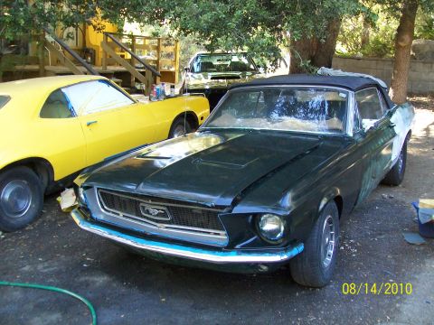 1968 Ford Mustang - 1968 Ford Mustang convertible in dark green, parked next to a yellow car. Bodywork is in progress.