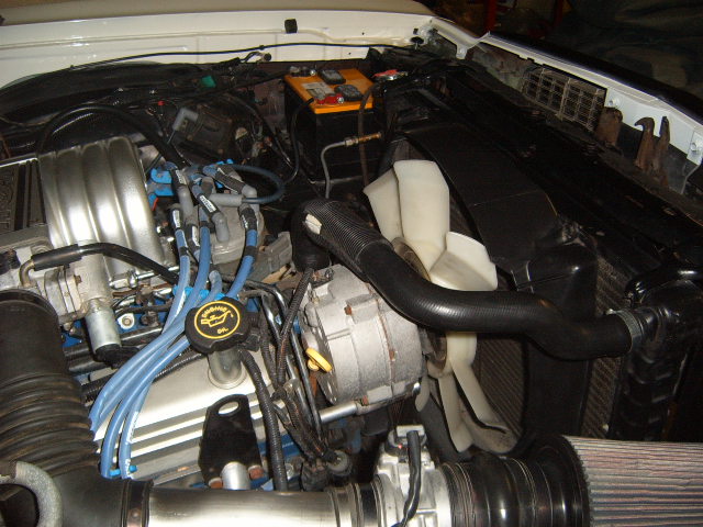close-up of a car engine bay with blue spark plug wires and a yellow oil cap