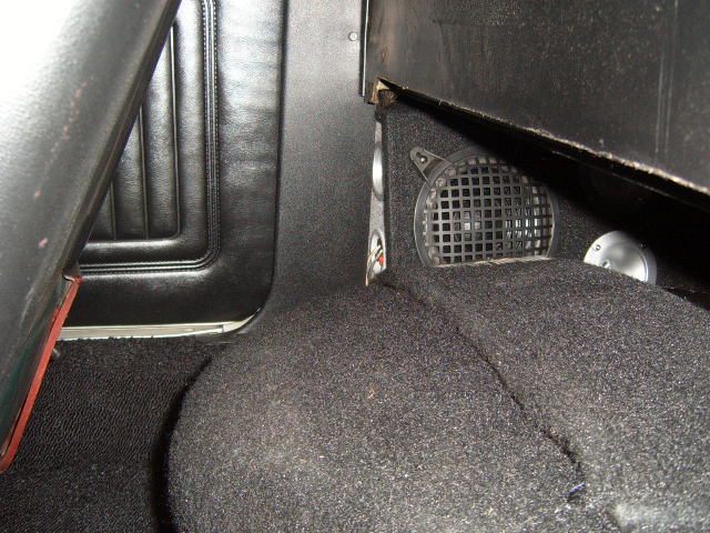 Close-up of a car's interior showing black carpet, a speaker grille, and part of a seat