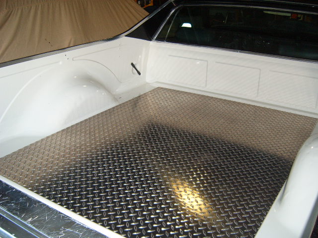 Diamond plate bed liner in white pickup truck bed. Supermotors.net logo visible