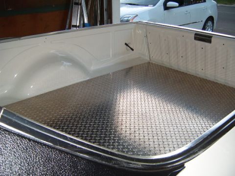 1973 Ford Ranchero - The interior of a truck bed is shown with diamond plate flooring, and a white sedan is parked behind it.