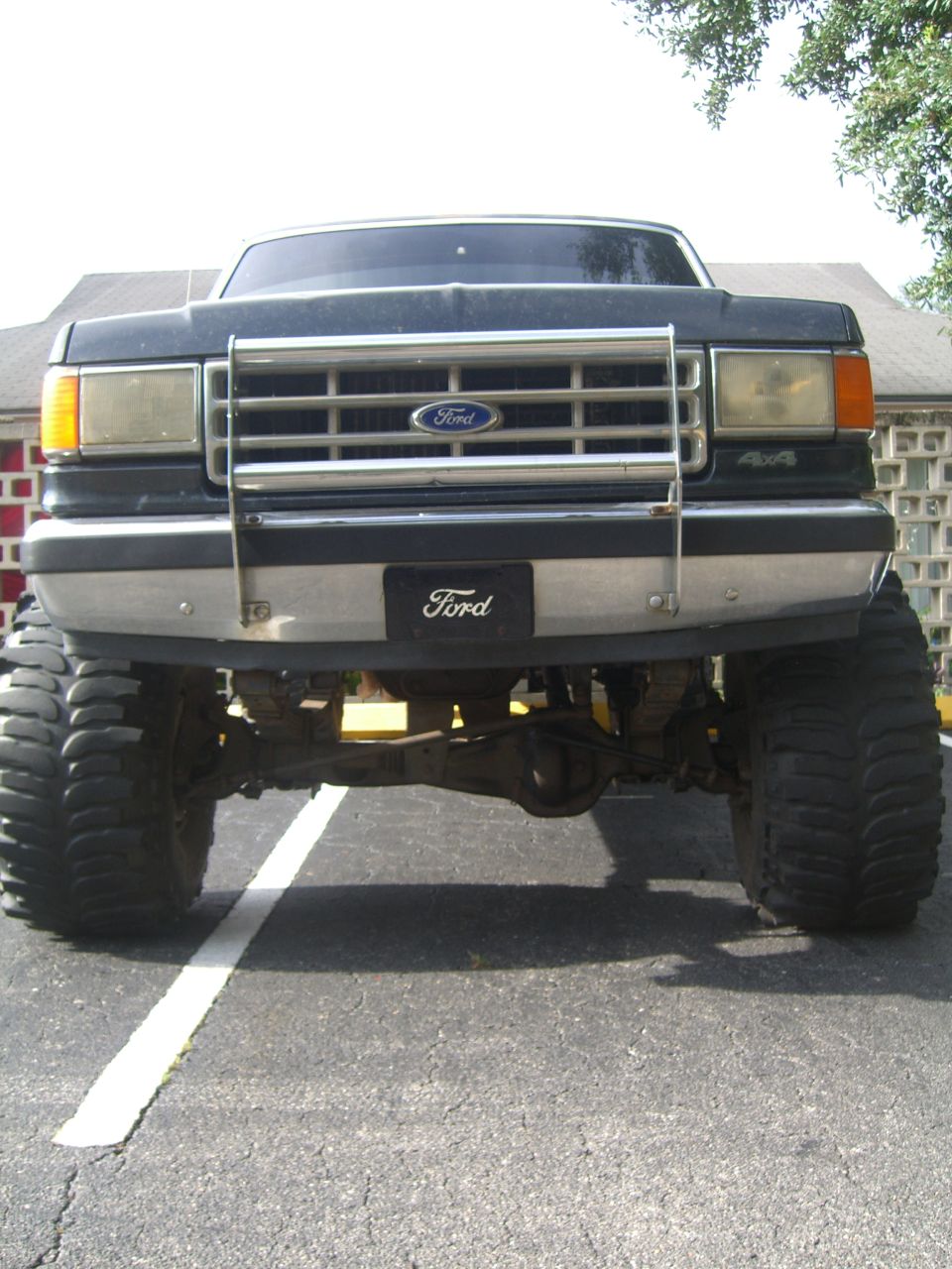 Front view of a lifted 1987 Ford F-250 with large off-road tires and a chrome grille guard