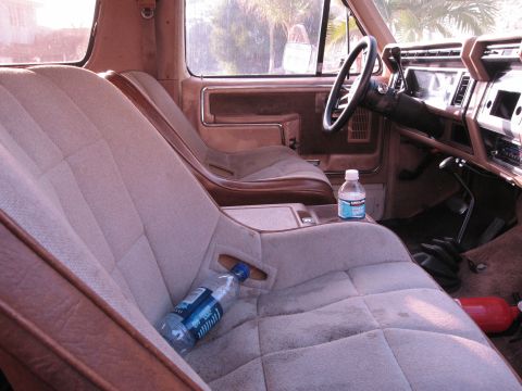 1986 Ford Bronco - The interior of a vehicle shows plush bucket seats and a center console with a gear shifter and cup holders.