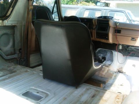 1986 Ford Bronco - The interior of a vehicle is shown with seats removed and the dashboard exposed, with another vehicle visible through the windows.