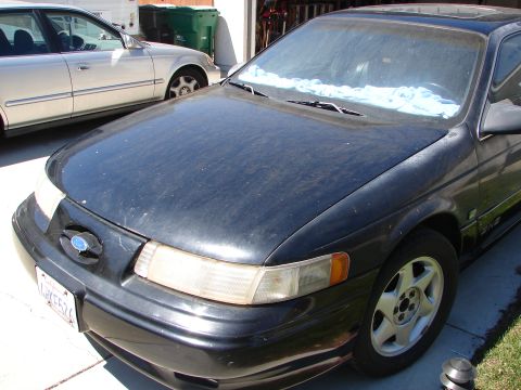1992 Ford Taurus - The front end of a black 1992 Ford Taurus is visible, parked next to another vehicle.