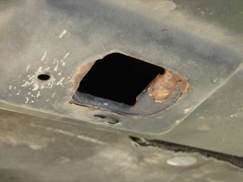 1992 Ford Taurus - Underside view of a vehicle showing a rusted opening with a black void behind it.