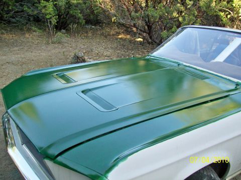 1968 Ford Mustang - A 1968 Ford Mustang hood is shown with a fresh green paint job over a white body, with a Supermotors watermark visible.