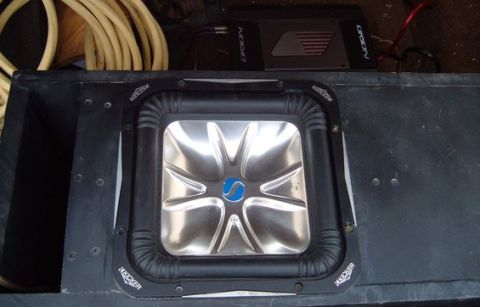 2006 Ford E350 - Overhead view of a square Kicker Solo-Baric subwoofer with a chrome dish cone mounted in a black carpeted enclosure, with an Orion amplifie…