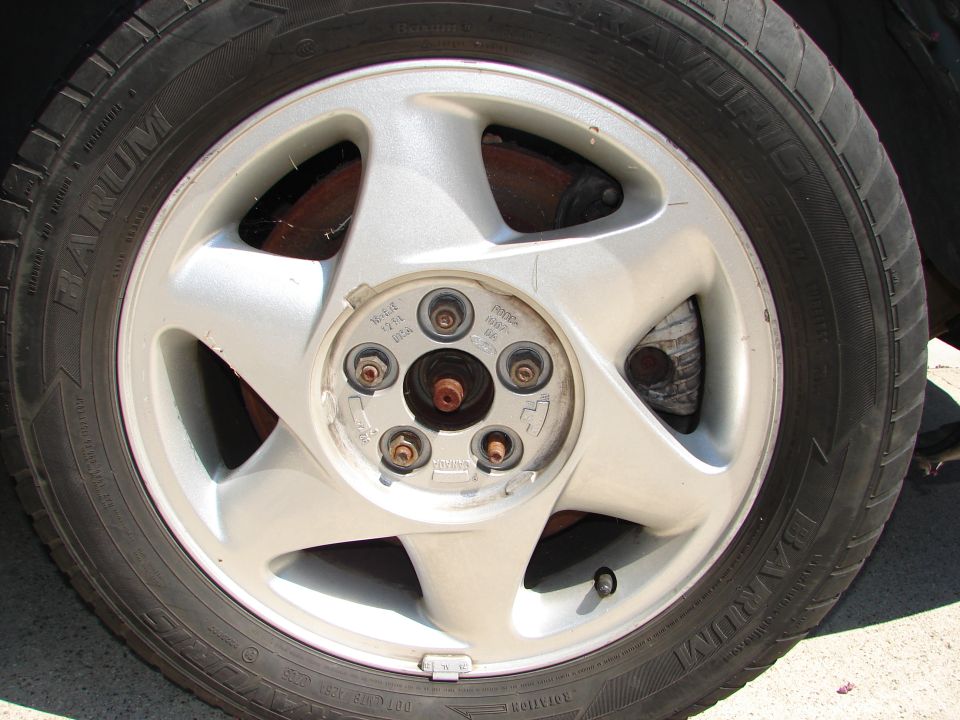 Silver five-spoke alloy wheel with a black tire, showing brake components and lug nuts