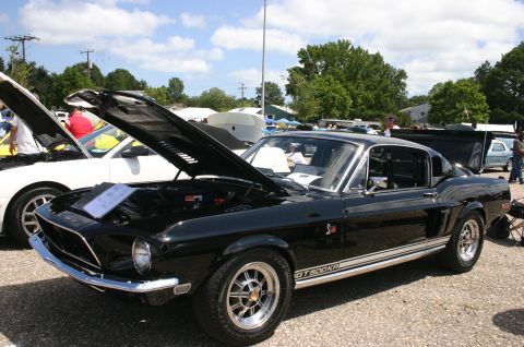 1968 Shelby GT500 - A black 1968 Shelby GT500KR is displayed with its hood open at a car show, alongside other vehicles.