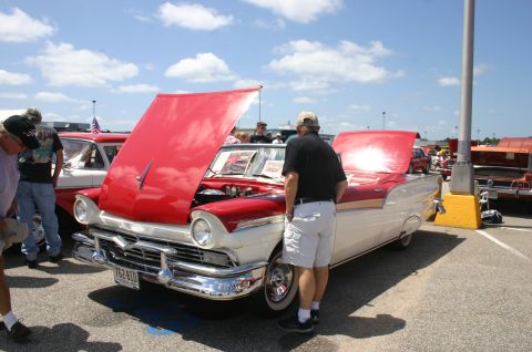1968 Shelby GT500 - A red and white 1957 Ford Fairlane 500 convertible is displayed with its hood open at a car show.