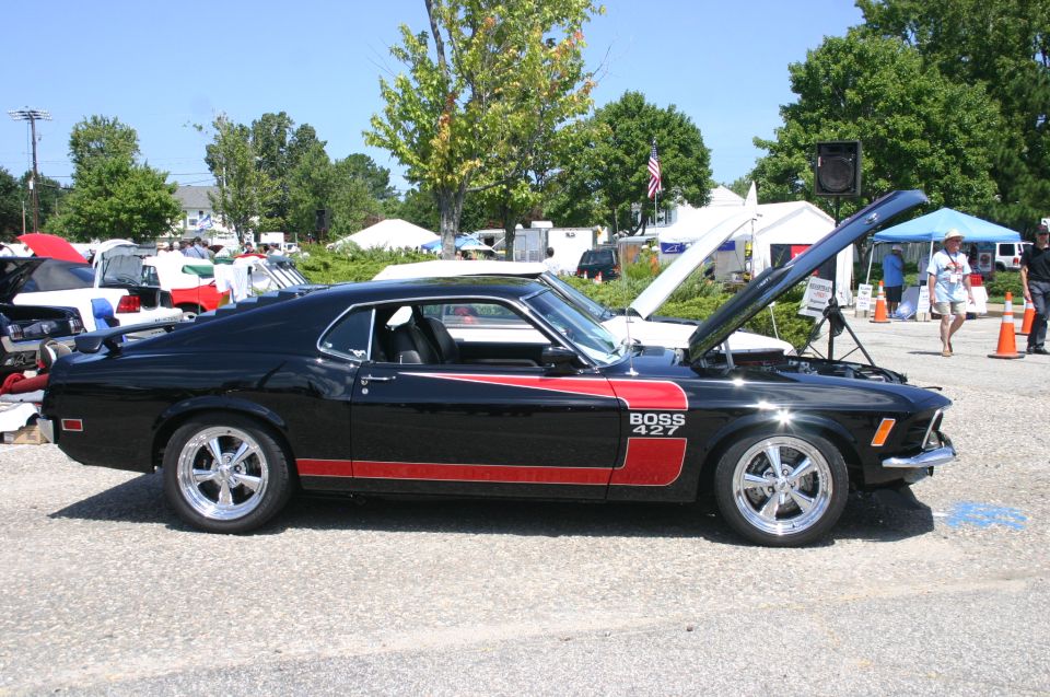 Black 1969 Ford Mustang Boss 427 with red stripe and hood open, parked at an outdoor car show