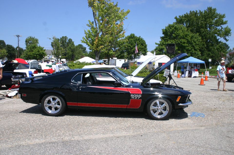 Black 1969 Ford Mustang Boss 427 with red side stripes and chrome wheels, hood open, parked outdoors at a car show