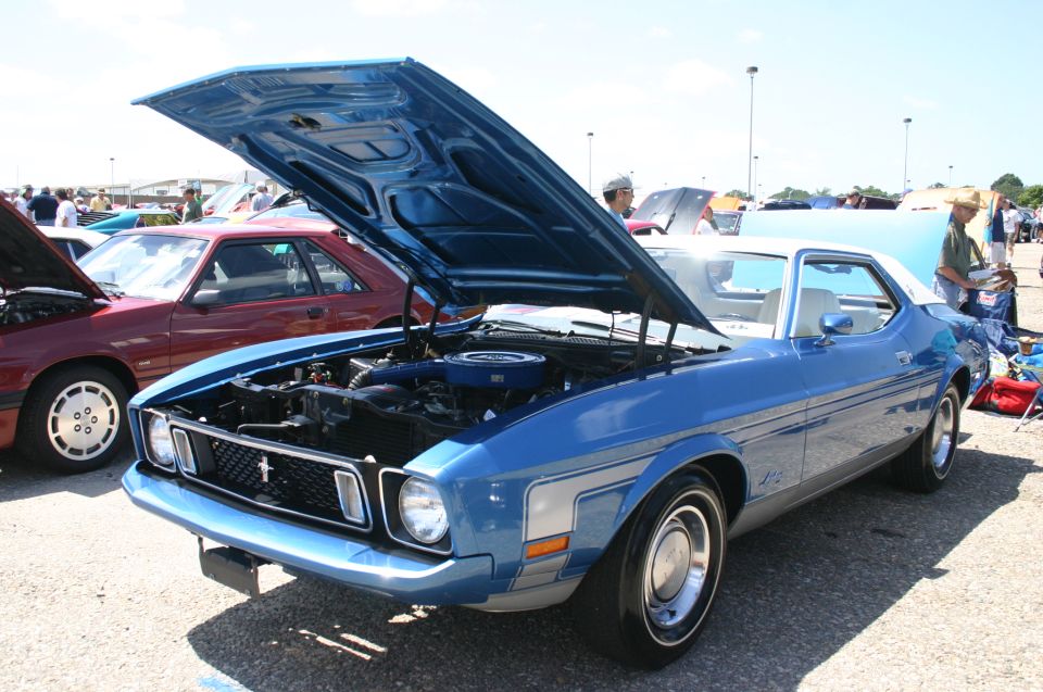 Blue and white 1971 Ford Mustang coupe with hood open, showing engine. Parked outdoors at a car show