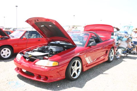 1968 Shelby GT500 - Two red Ford Mustangs are parked side-by-side at an outdoor car show.
