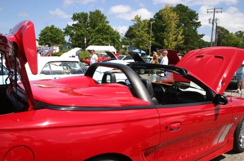 1968 Shelby GT500 - A red convertible is displayed with its hood and trunk open at a car show, with other vehicles and people in the background.