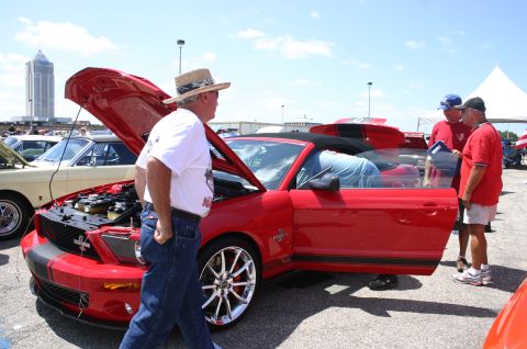 1968 Shelby GT500 - A red convertible car with racing stripes is displayed with its hood and doors open at an outdoor car show.