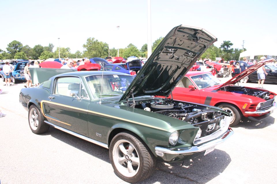 Green 1969 Ford Mustang with hood open, parked next to a red 1970 Ford Mustang with hood open