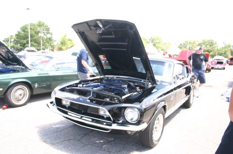 1968 Shelby GT500 - A black 1968 Shelby GT500 is displayed with its hood open at a car show, revealing the engine bay.