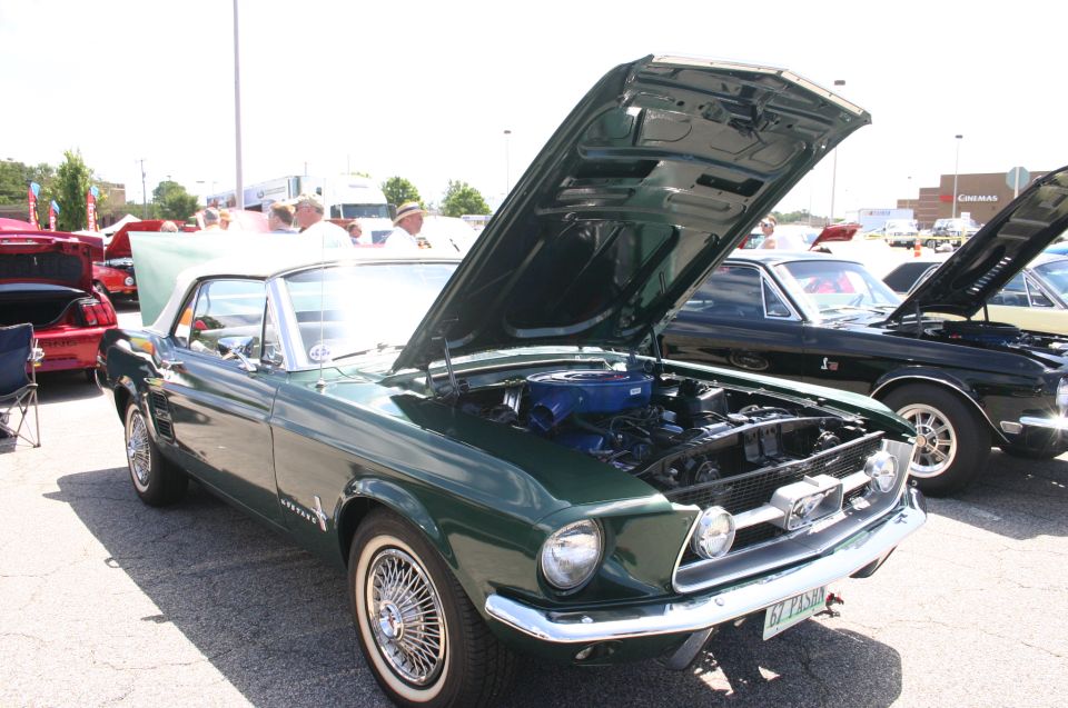 Green 1967 Mustang convertible with hood open, showing engine. Another Mustang is parked next to it