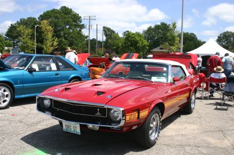 1968 Shelby GT500 - A red convertible with a white top and yellow stripe is parked at an outdoor car show.
