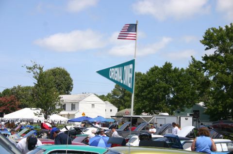 1968 Shelby GT500 - An outdoor event with numerous cars, tents, and flags, suggesting a car show or gathering.