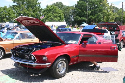 1968 Shelby GT500 - A red 1969 Ford Mustang Mach 1 is displayed with its hood and driver's door open at an outdoor car show.