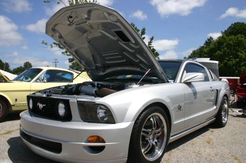 1968 Shelby GT500 - A silver 2005 Ford Mustang GT is displayed with its hood open, alongside an older yellow Mustang.