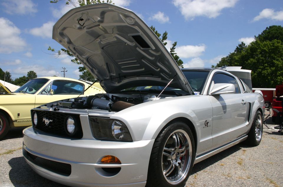 Silver 2005 Ford Mustang GT with hood open, parked next to a yellow 1960s Ford Mustang