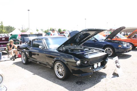 1968 Shelby GT500 - A black classic car with its hood open is displayed at an outdoor car show, with other vehicles visible in the background.