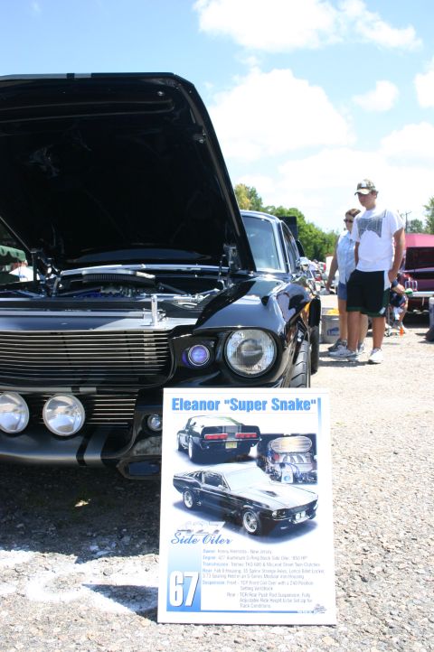 1968 Shelby GT500 - A black 1967 Ford Mustang Eleanor "Super Snake" is displayed with its hood open, next to a descriptive sign.