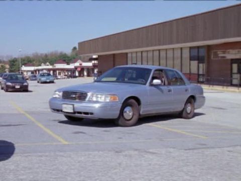 2000 Ford Crown Victoria - A silver sedan is parked in a lot in front of a building.