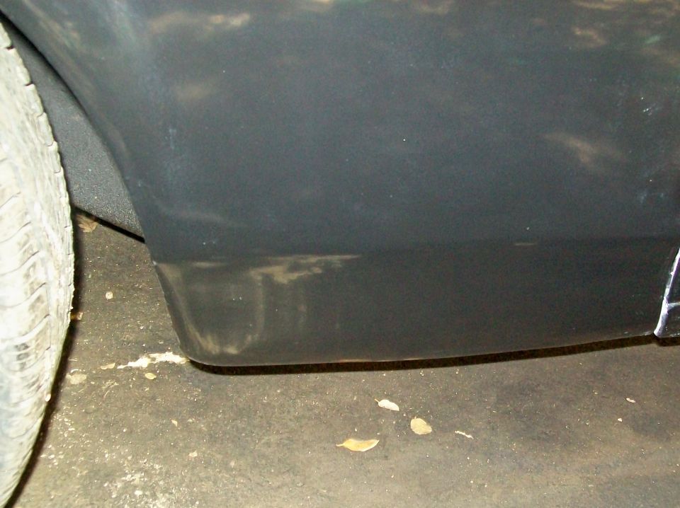 Close-up of a dark-colored vehicle's rear fender and tire. Some dirt and debris on the ground