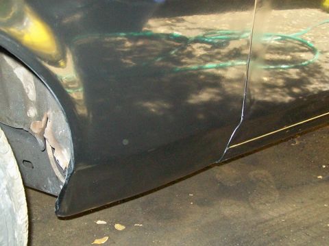 1972 Ford Ranchero - Close-up of a dark-colored vehicle's side panel shows evidence of bodywork and a damaged fender area.
