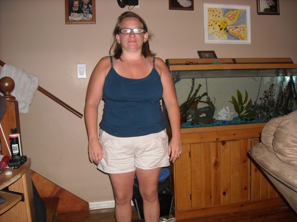 woman in tank top and shorts stands in front of a large aquarium