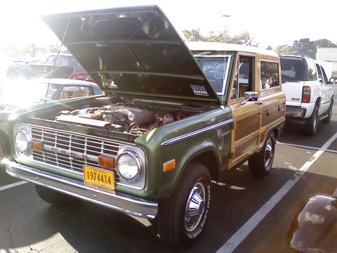 1989 Ford Bronco - 1974 Ford Bronco with woodgrain trim and hood open, parked next to a GMC SUV.