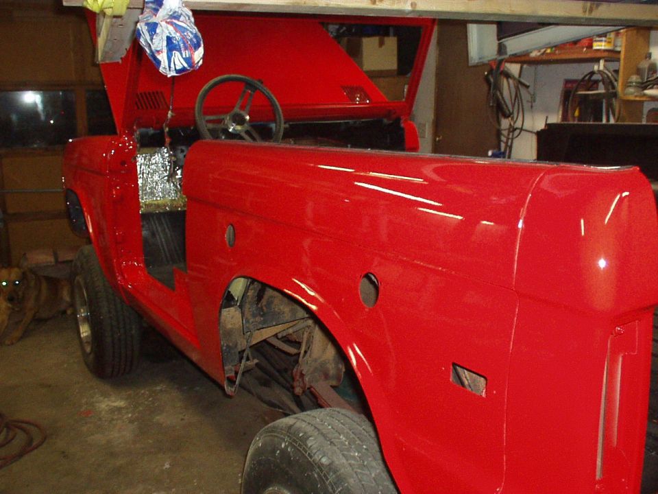 Red 1973 Ford Bronco body with hood open, undergoing restoration