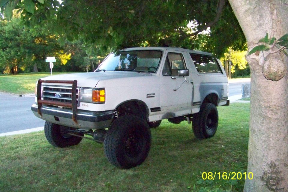 Lifted white Ford Bronco with tube grille guard parked on grass under a tree