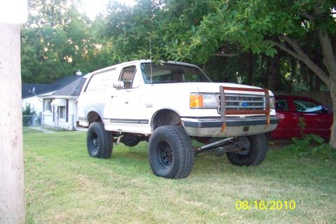 1989 Ford Bronco - This lifted 1989 Ford Bronco is parked on a grassy lawn next to a house.