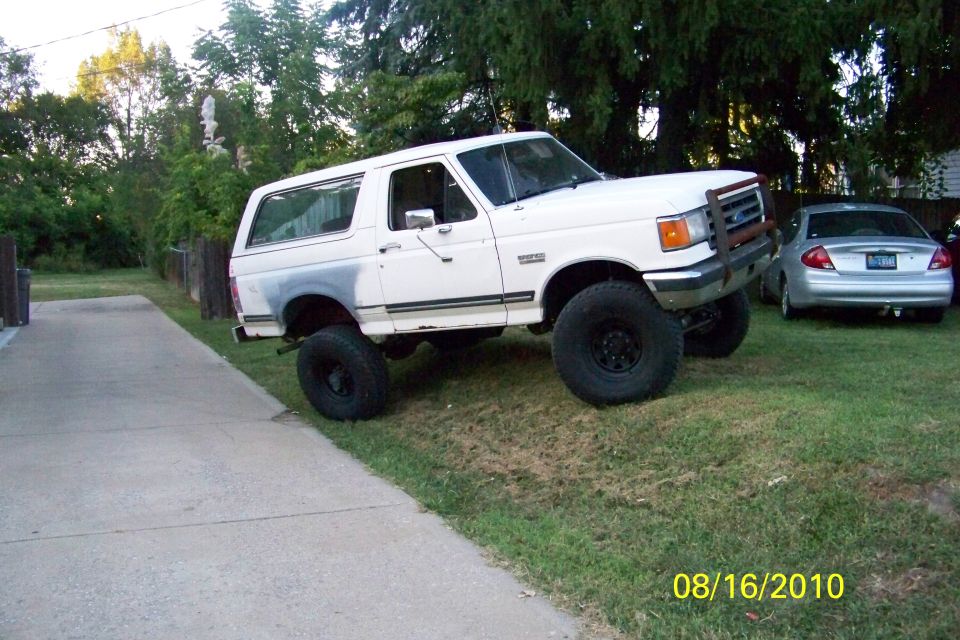 White 1989 Ford Bronco with large tires on grassy incline