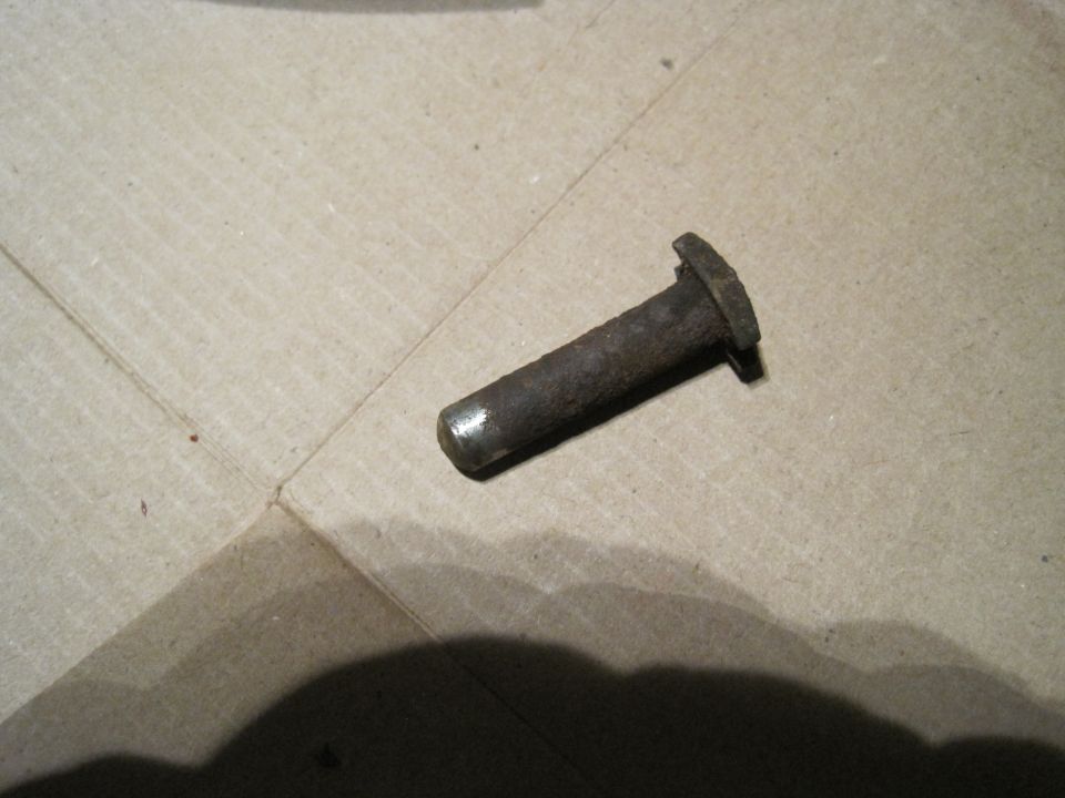 Rusty metal pin with a flat head and a cylindrical shaft resting on cardboard