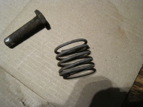 1979 Ford Bronco - A close-up view of a rusty metal pin and a coiled spring resting on a cardboard surface.