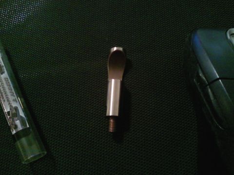 1990 Ford Bronco - A metal tool part with a threaded base and a flattened, curved tip is shown against a dark background.