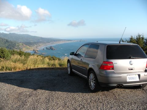 1991 Ford Bronco - A silver Volkswagen GTI is parked on a gravel overlook, with a scenic coastal view of the ocean and rocky outcrops.