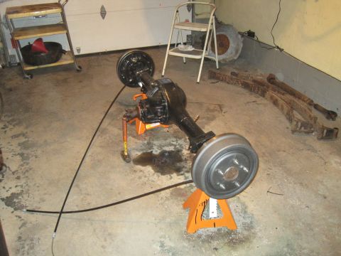 1979 Ford Bronco - A rear axle assembly with drum brakes is supported by orange jack stands in a garage setting.