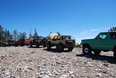 1996 Ford Bronco - A group of modified off-road vehicles are parked on a rocky incline with trees in the background.