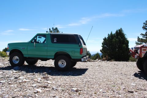 1996 Ford Bronco - A green SUV sits on a rocky terrain under a clear blue sky, with another vehicle partially visible to the right.