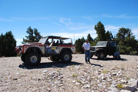 1996 Ford Bronco - Two off-road vehicles are parked on a rocky surface under a clear blue sky, with trees in the background.