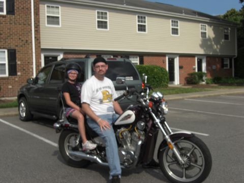 1986 Honda Shadow Aero - A man and child sit on a motorcycle in a parking lot, with a dark SUV behind them.